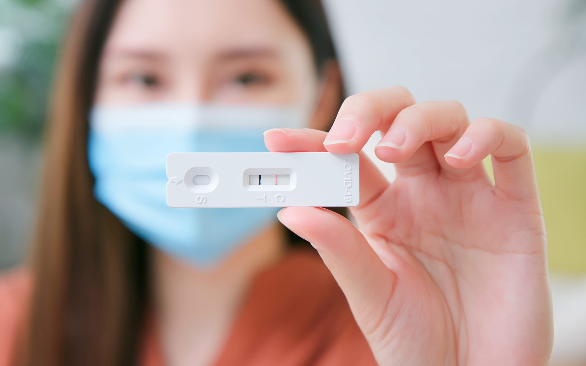masked woman holds positive covid 19 test