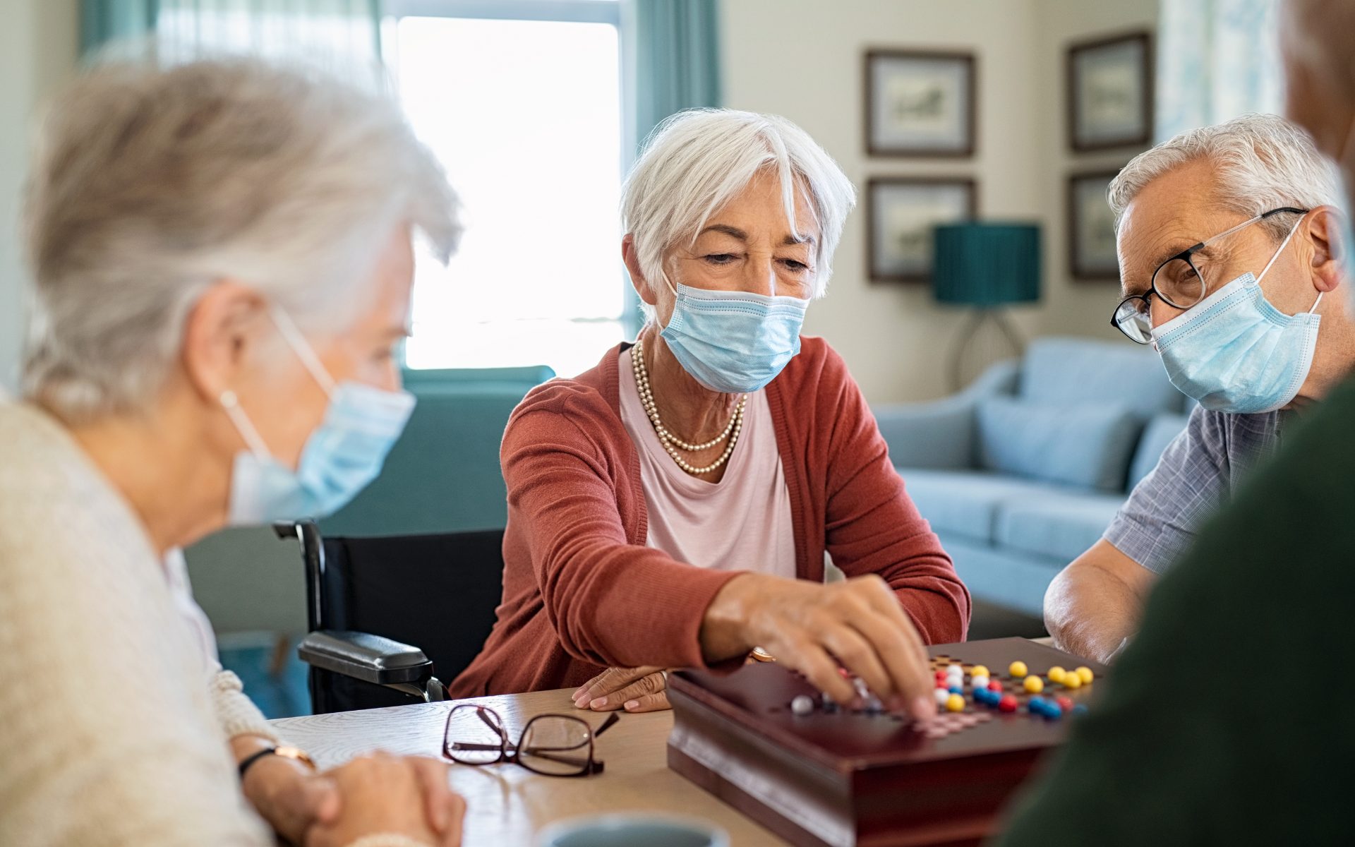 masked senior friends play chinese checkers together in care home