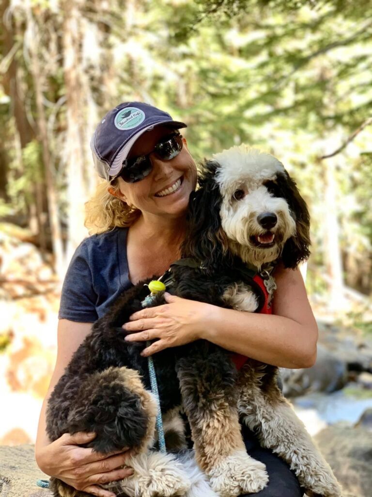 a smiling woman with her dog out in the woods
